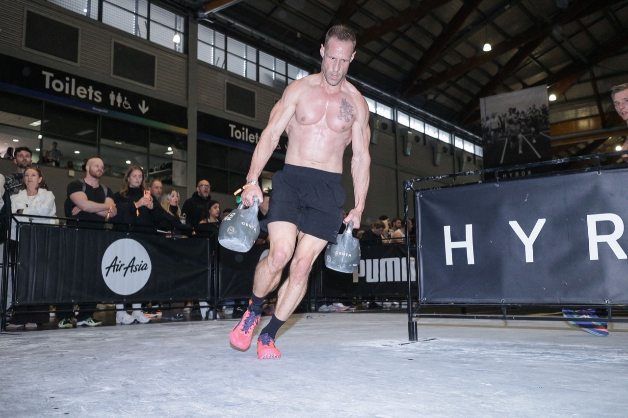 Tyson Schubert carrying two kettlebells during the farmers carry at HYROX Sydney