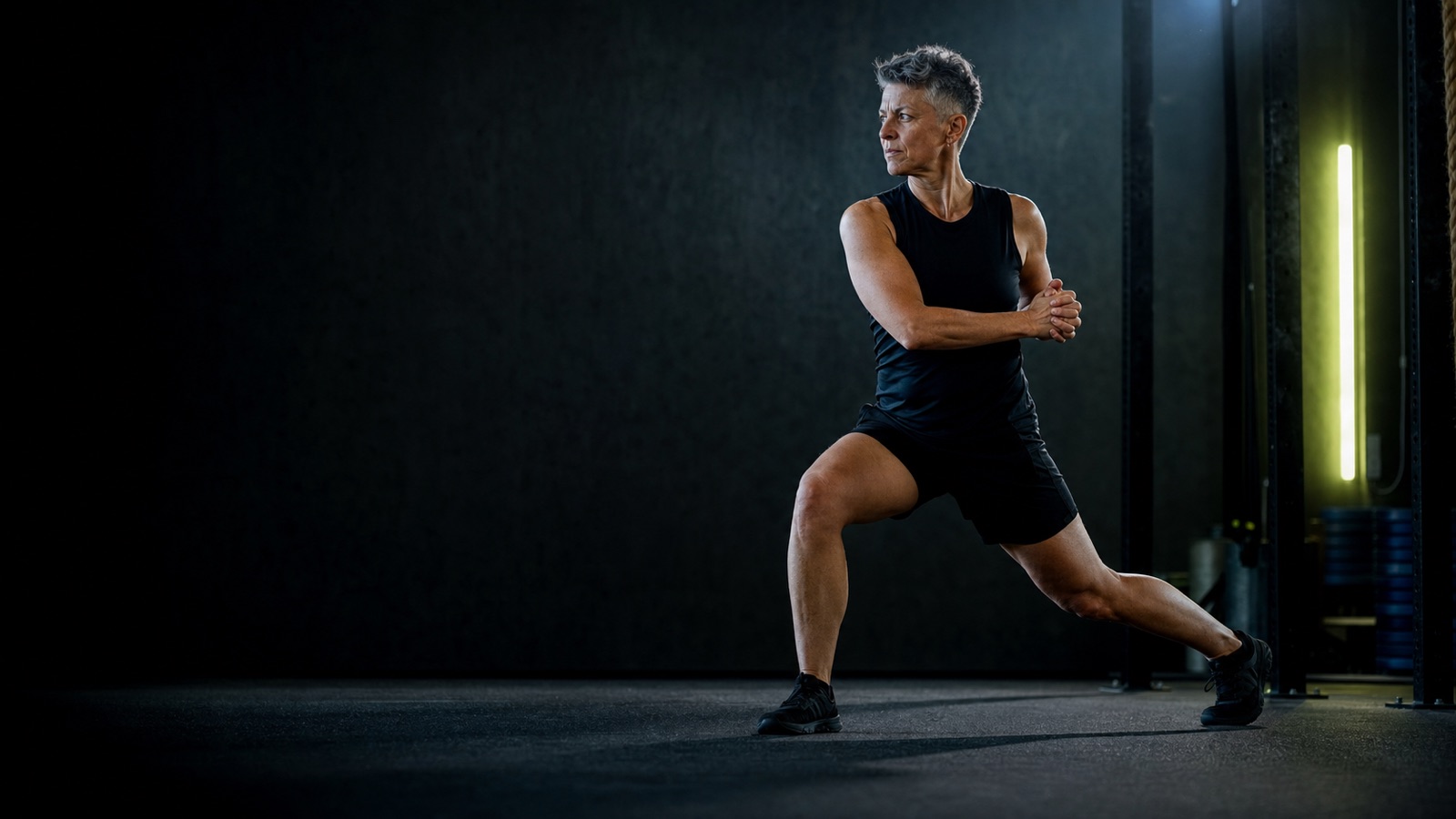 Mature athlete performing a controlled split-stance rotation in a dark training space